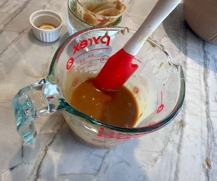 Red spatula in a clear liquid measuring cup stirring a brownish liquid mix