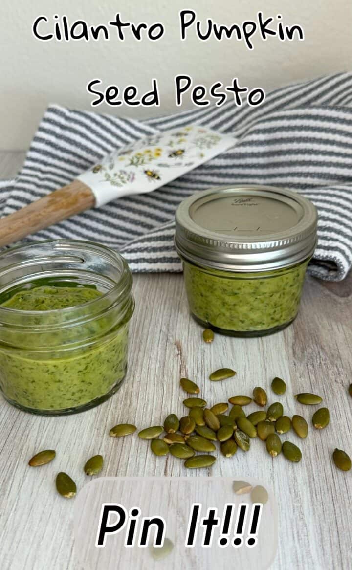 Close up of two small jars of green pesto with spatula and striped dish towel plus pumpkin seeds and text.