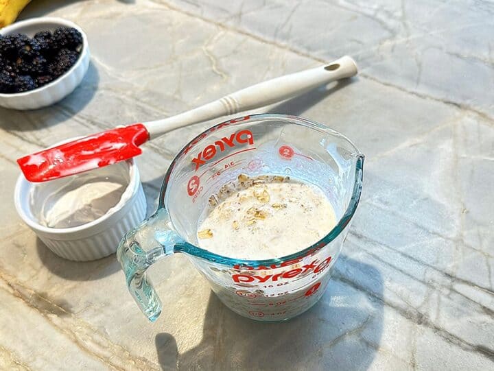 Measuring cup full of oats, milk, and yogurt with the red spatula used to mix off to the side.