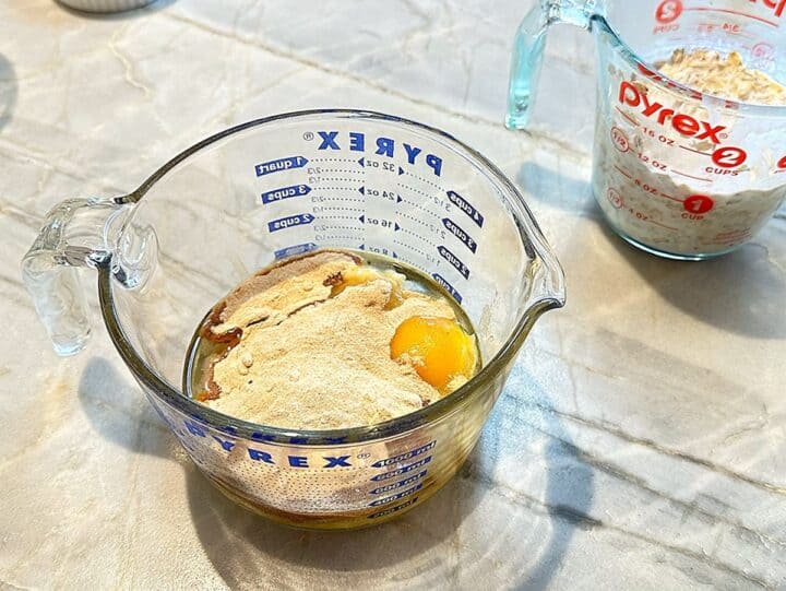 Raw egg and other wet ingredients for muffins with date sugar on top in a large capacity glass measuring cup.
