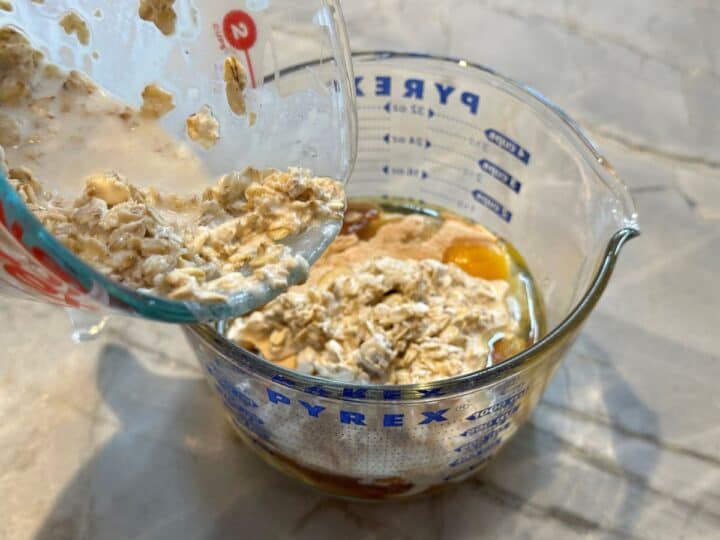 Adding oats soaked in yogurt-milk mixture to an oversize measuring cup with raw egg and other wet ingredients.