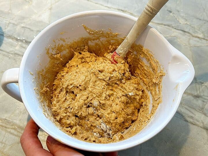 Lumpy, golden-colored batter in a white bowl with the handle of a  wooden visible that was used for mixing.