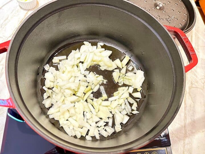 White chopped onions cooking in oil in a red pot with black interior