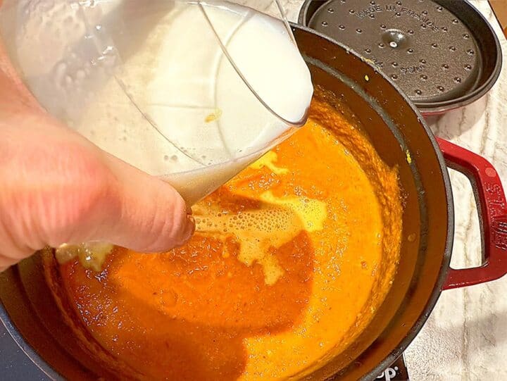 Pouring milk into a pot containing orange pumpkin soup base.